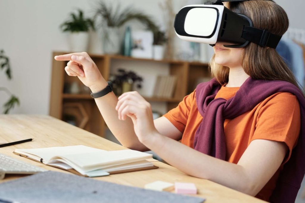 Girl in orange shirt making calculations with her finger in the air using virtual reality goggles to learn.