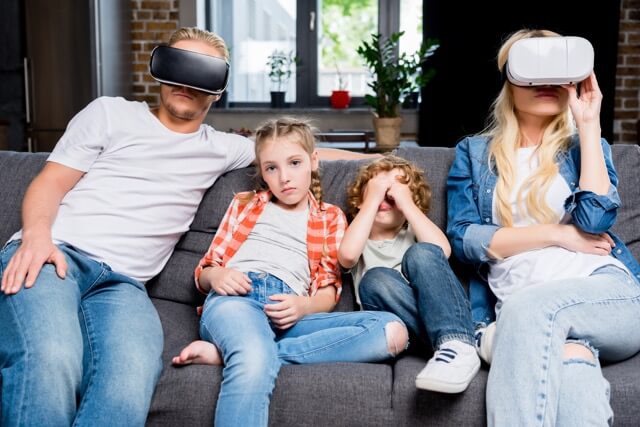 Mom and Dad wearing Virtual Reality headsets on the Sofa with kids, ignoring the two children.